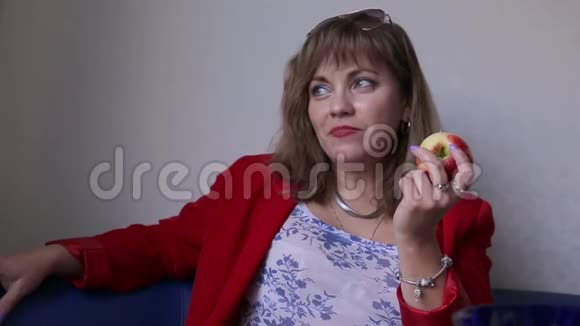 漂亮的女人在室内吃苹果健康的食物概念穿红色衣服的女人在中性背景下特写视频的预览图