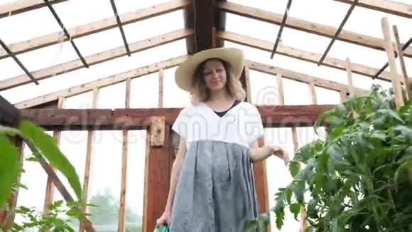 戴着草帽穿着草裙的微笑着的女农民带着浇水罐去了温室视频的预览图