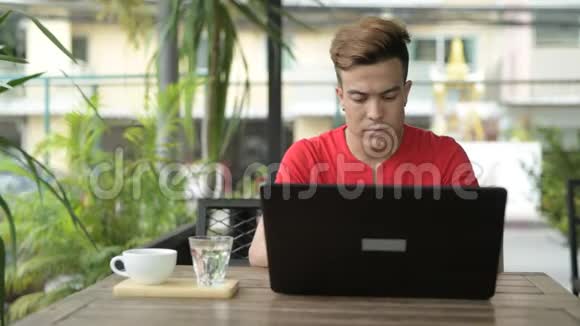 快乐的亚洲年轻人在户外咖啡店用笔记本电脑视频的预览图