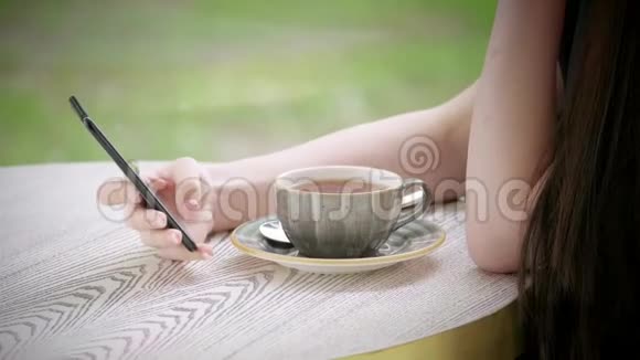 身体的一部分年轻的高加索女孩手里拿着智能手机桌上的茶杯咖啡台视频的预览图