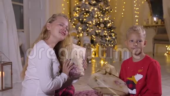 青少年女孩和男孩在节日树背景上拿着新年礼物盒视频的预览图