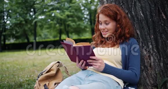 快乐的红头发女孩在公园户外看书微笑着在草地上放松视频的预览图