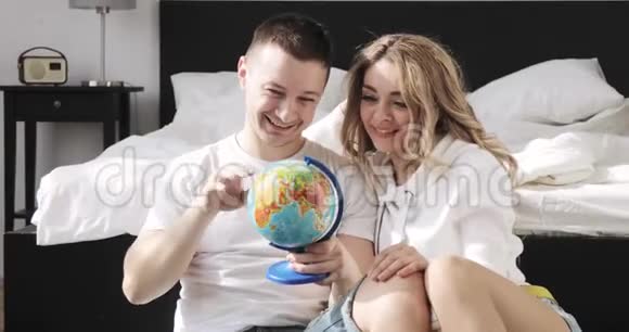 幸福的爱人坐在床边的男人和女孩正在看着环球选择了蜜月旅行的地方视频的预览图