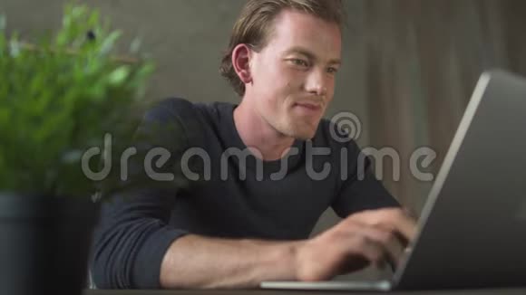 微笑的商务年轻人坐在电脑前在笔记本电脑上打字帅哥商人发短信说视频的预览图