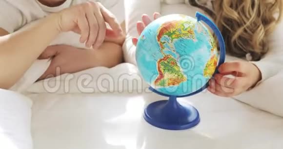 床上不可辨认的一对夫妇正在看着地球旋转它并指向随机选择一个地方旅行视频的预览图