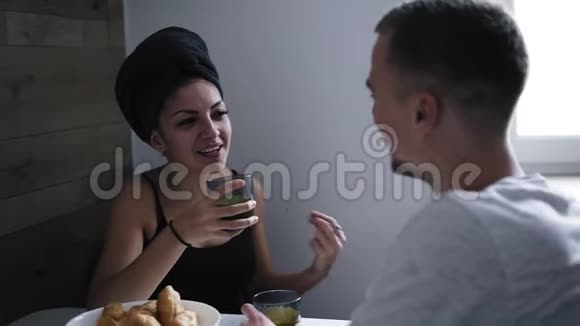 美丽的女人淋浴后头上戴着深色毛巾吃羊角面包喝咖啡在和她男朋友说话视频的预览图