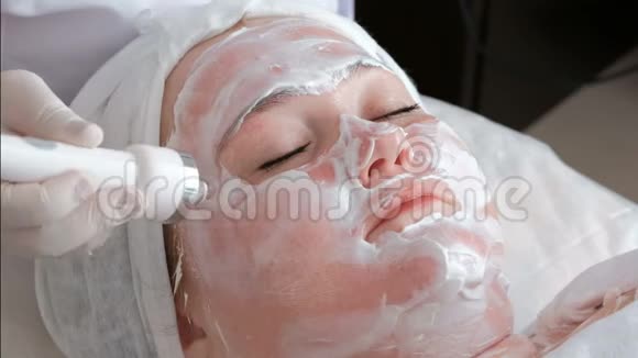 一个女人闭着眼睛在美容院的治疗过程中脸上涂上奶油专业的美容师或视频的预览图