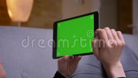 特写后景拍摄女性双手捧着平板电脑绿色屏幕躺在舒适的室内沙发上视频的预览图