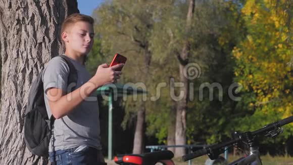 骑自行车后在公园里的男孩在日落时使用电话观看社交网络或聊天健康观念视频的预览图