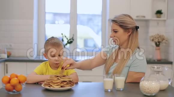 白种人金发男孩和年轻妈妈玩得很开心年轻的母亲戏弄男孩煎饼快乐的家庭早餐视频的预览图
