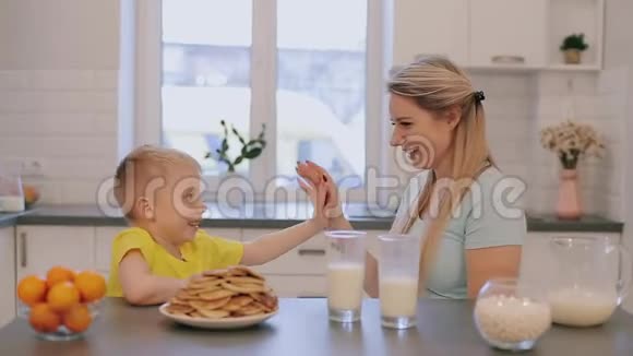 快乐美丽的白种人母亲和她的儿子在白色的厨房里玩给他击掌视频的预览图