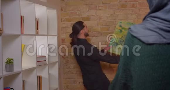 一对年轻迷人的穆斯林夫妇在室内新买的公寓里安顿下来的特写镜头一个男人把照片挂在视频的预览图