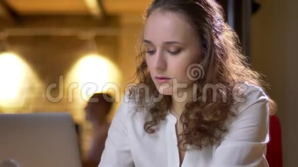 一位年轻的卷发女士的特写肖像她专心地用笔记本电脑和办公室里的饮料工作视频的预览图