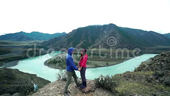 一对游客正站在石山上玩着玩着拥抱着一条湍急的山河在下面流淌视频的预览图