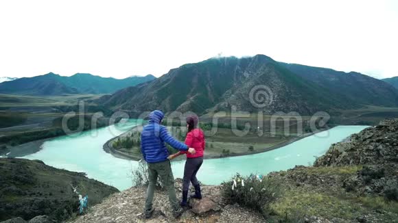 几个游客正站在一座石山上拥抱下面是一条湍急的山河背面视频的预览图
