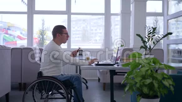 商务自由职业者轮椅残废的老人戴着眼镜使用手机坐在笔记本电脑上工作视频的预览图