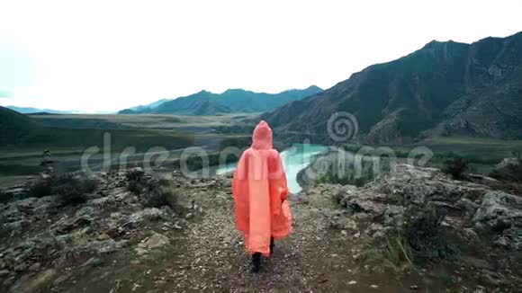 穿着橙色雨衣的女旅行者来到山崖边背面视频的预览图