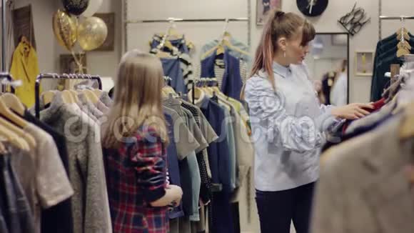 年轻漂亮的女售货员试图帮助她的成年女性顾客找到一些漂亮的衣服并给她一件t恤视频的预览图