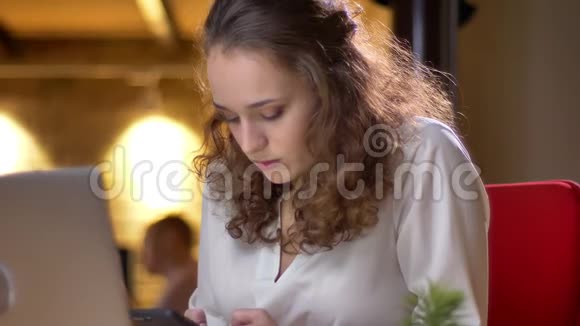 年轻的卷发女商人在办公室里体贴地在智能手机上打字的特写肖像视频的预览图