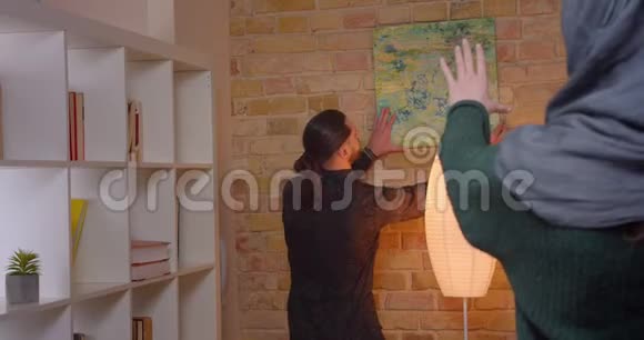 一对年轻迷人的阿拉伯夫妇在室内新买的公寓里安顿下来的特写镜头一个男人把照片挂在视频的预览图
