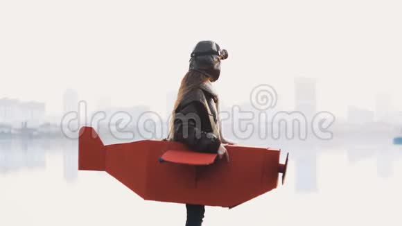 快乐的小飞行员女孩站在惊人的湖城全景播放飞行员在纸板飞机运行缓慢的运动视频的预览图