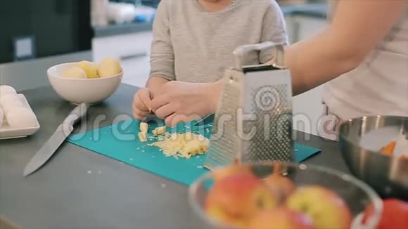 妈妈切奶酪在厨房里送给儿子年轻的母亲可爱的漂亮儿子大眼睛做饭视频的预览图