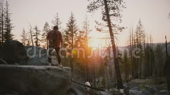 成功的年轻男性博客写手从一块大森林石头上跳下来在令人惊叹的约塞米蒂公园日落慢动作上爬上岩石视频的预览图
