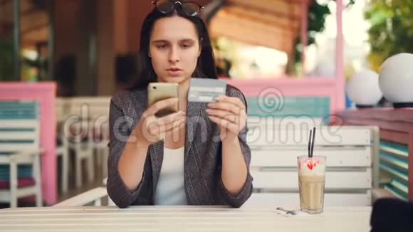 漂亮的年轻女人拿着银行卡和智能手机在网上支付触摸屏幕然后微笑互联网视频的预览图