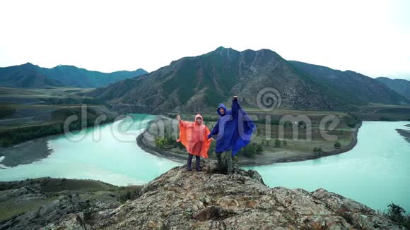 两个穿着雨衣的恋人站在山的边缘挥舞着手臂背面视频的预览图