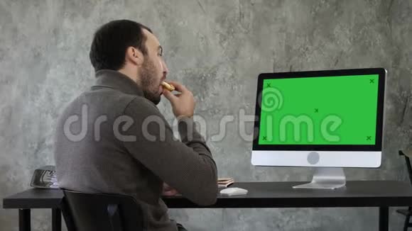 年轻人一边吃东西一边在办公室里看电脑上的东西绿色屏幕模拟显示视频的预览图