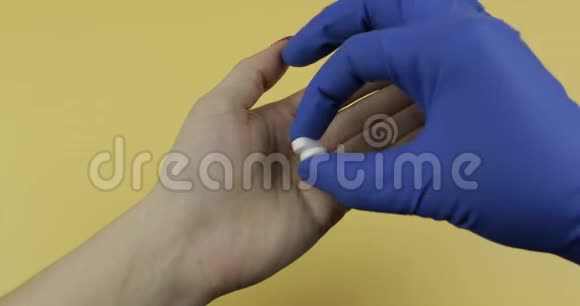 穿着蓝色医用手套的手把两颗白色药丸放进女人的手里视频的预览图