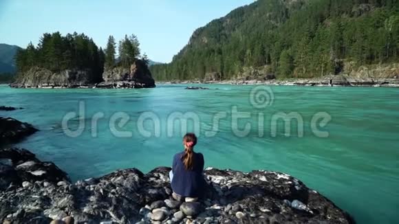 穿毛衣的女孩坐在河边美丽的风景背面视频的预览图