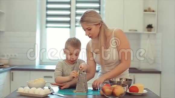 一位年轻美丽的白种人母亲留着白发儿子在明亮的厨房做饭妈妈教儿子做饭视频的预览图