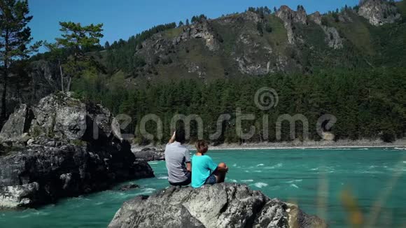 两个年轻人坐在快山河旁合影留念背面视频的预览图