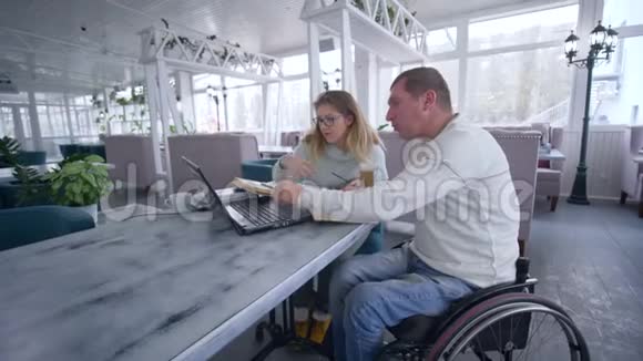 在轮椅上工作的男子餐厅业主中有一名妇女使用笔记本电脑进行规划和管理视频的预览图