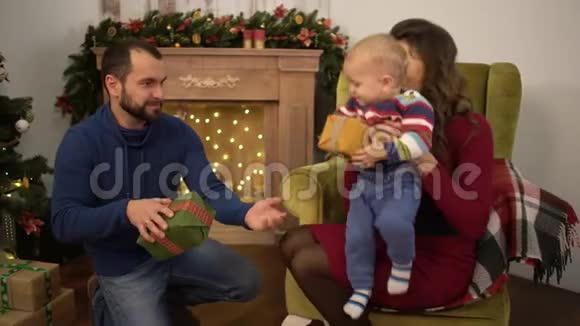 母亲父亲和小婴儿坐在房间里装饰着圣诞节那个人把小礼物盒给了视频的预览图