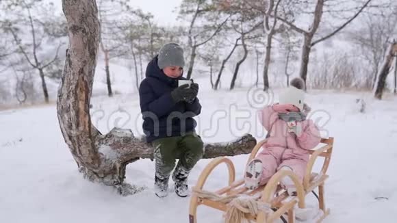 男孩喝茶女孩吃圣诞姜饼穿着连衣裙后雪天雪橇兄弟姐妹冬天视频的预览图