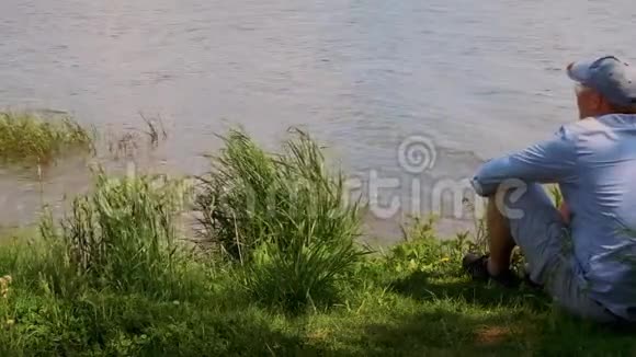 戴帽子的人坐在湖边的一棵树下喝水视频的预览图