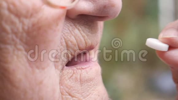 老年妇女服用白色药丸以减轻其健康问题的概况祖母在户外把药片放进嘴里视频的预览图