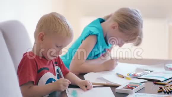 男孩和女孩一起在家里的书桌上用彩色铅笔在纸上画画视频的预览图