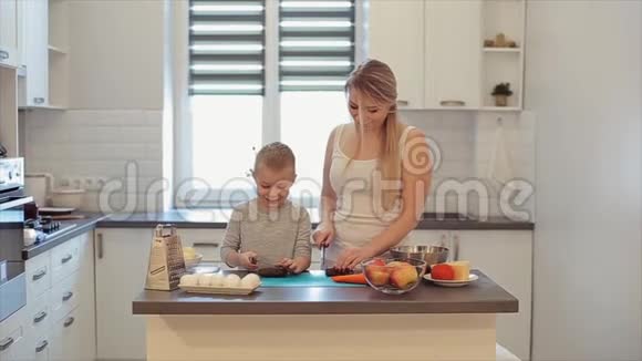 一位年轻美丽的白种人母亲留着白发儿子在明亮的厨房做饭妈妈教儿子做饭视频的预览图