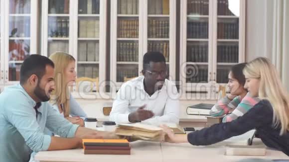 多种族的年轻人坐在桌子旁阅读参考书以作学习笔记在校青年学生群体视频的预览图