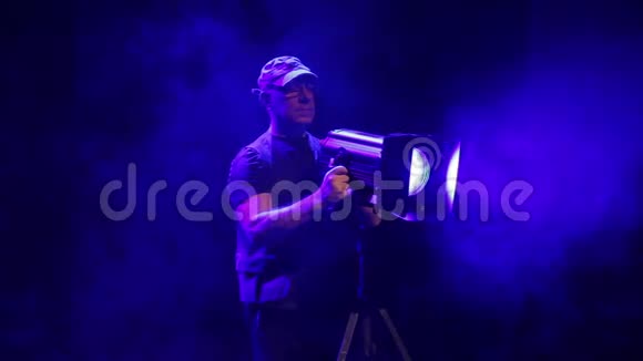 一个在舞台上工作的人用一台戏剧轮廓投影仪引导烟雾中的光线视频的预览图