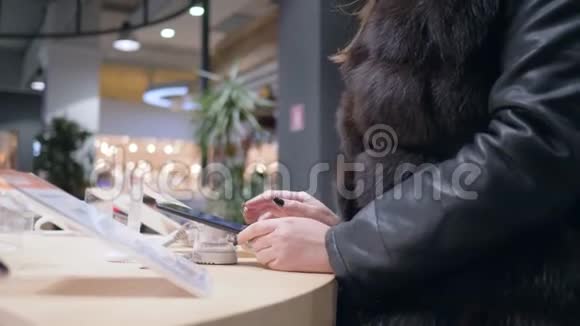 穿毛皮衣服的女性购物者选择电子商店的现代智能手机视频的预览图
