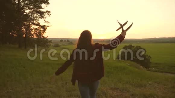 快乐的女孩在日落时带着玩具飞机在田野上奔跑快乐童年的概念孩子们玩玩具飞机少年少年少年视频的预览图