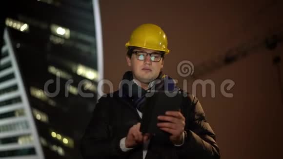 中镜头建筑师在黄色头盔中向前移动手持平板电脑视频的预览图