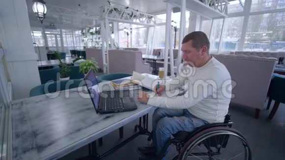 成功的无效餐馆老板轮椅上的男子使用现代计算机技术进行管理和开发视频的预览图
