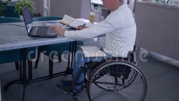 残疾成功患病学生的远程教育男性坐在轮椅上用手提电脑从网上学习视频的预览图