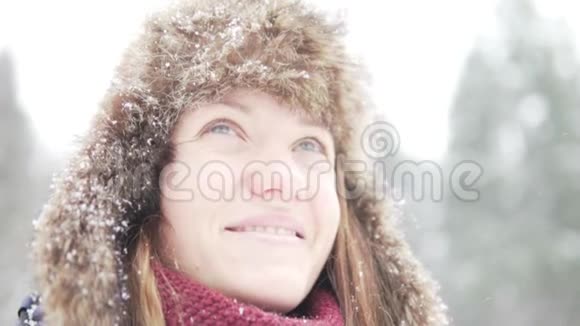 一个戴着暖和的冬帽戴着耳罩的年轻女子望着飘落的雪视频的预览图