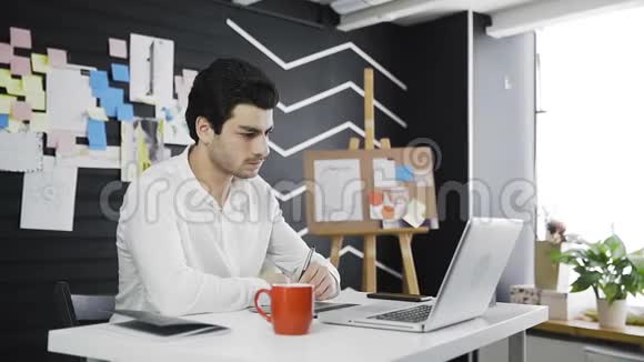 休闲男性设计师在现代办公室里喝咖啡和使用图形平板电脑视频的预览图